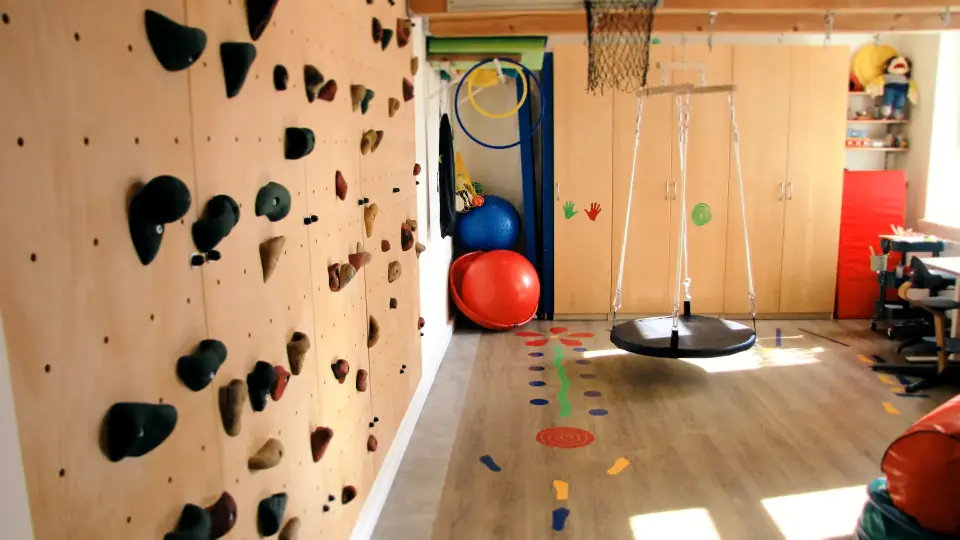 Therapieraum der Praxis mit Kletterwand, Schaukel und Bällen